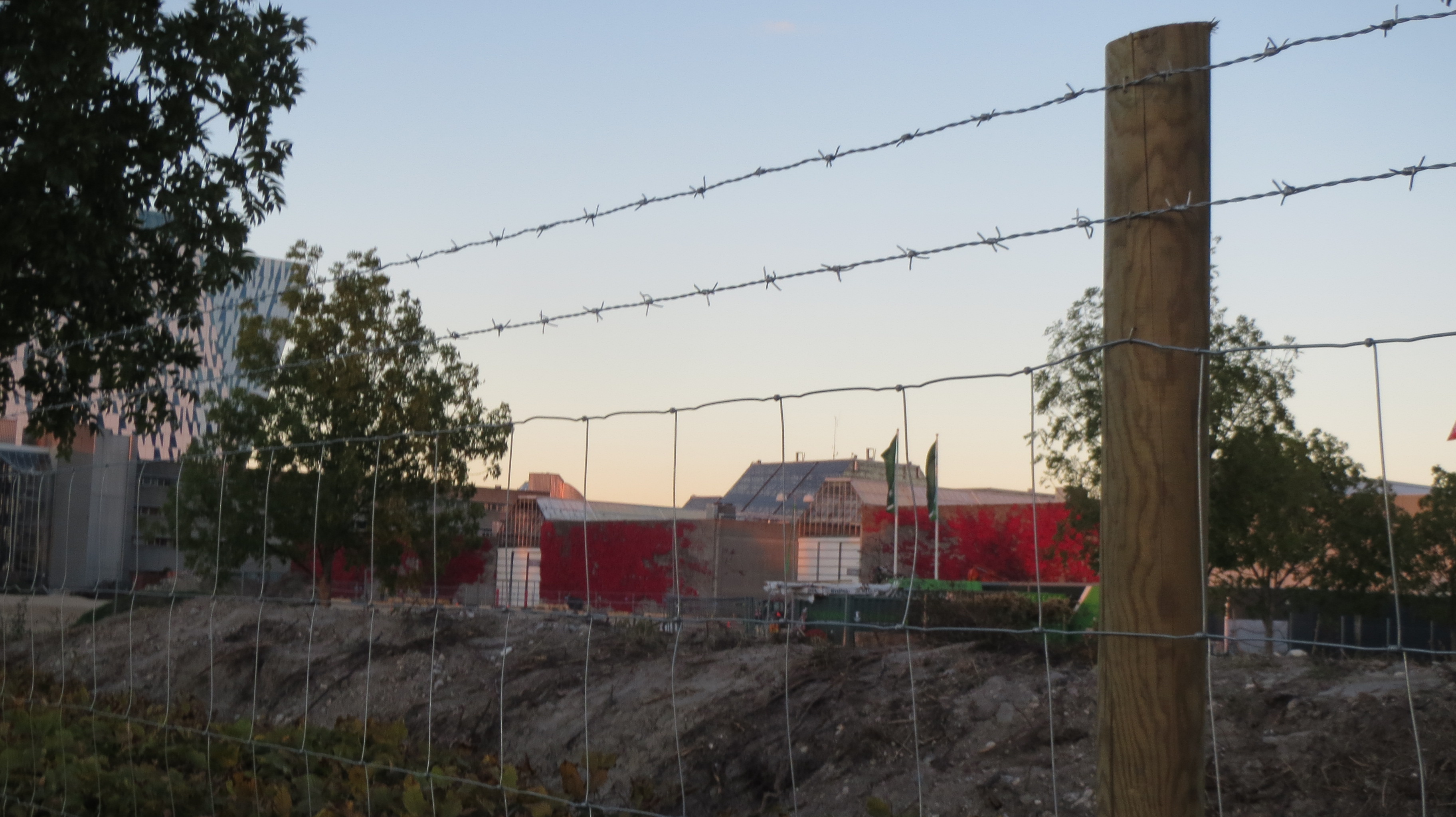 I baggrunden ses en rød bygning, i forgrunden ses et byggepladshegn