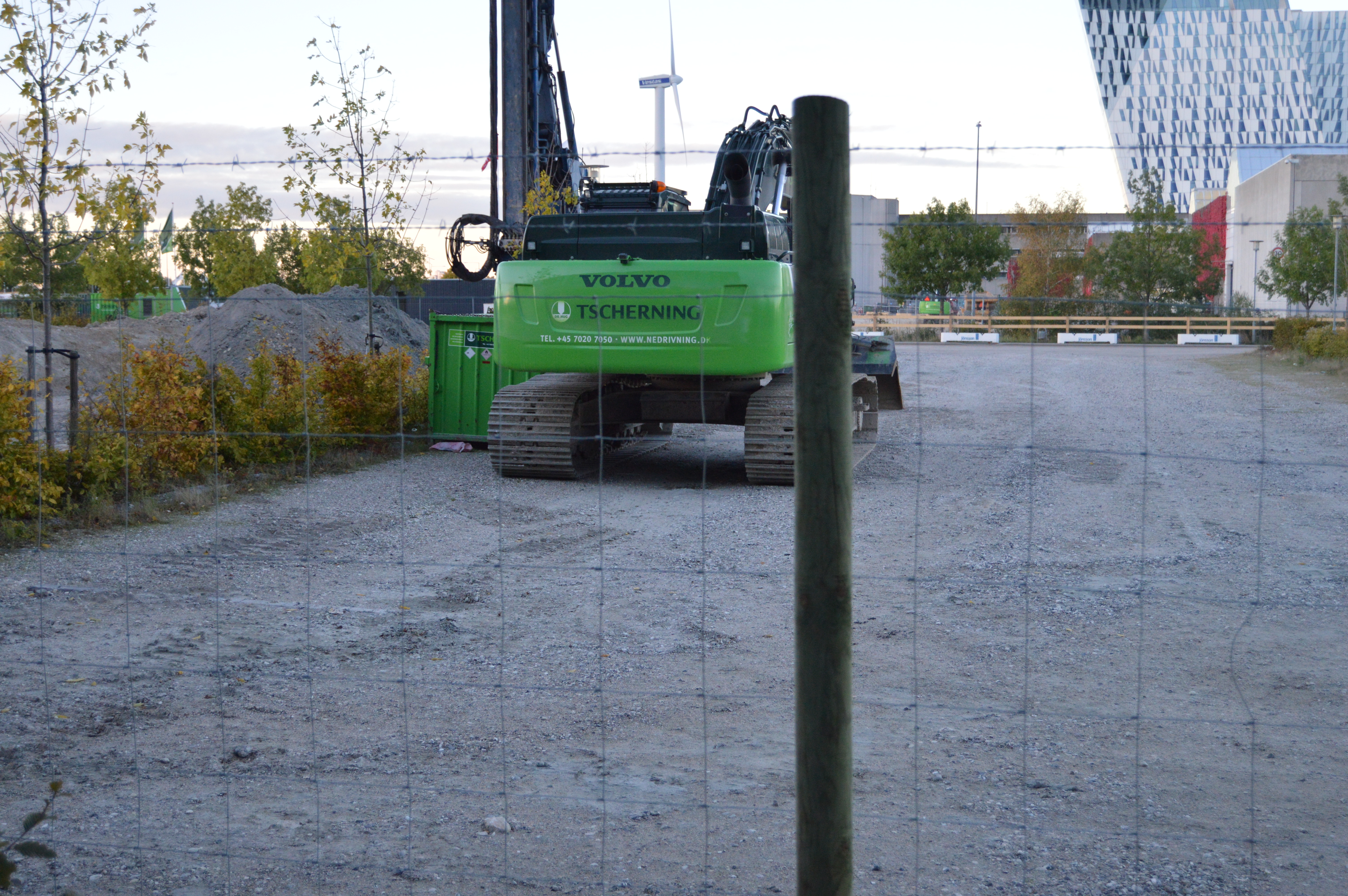 I forgrunden ses et byggepladshegn. Bagved hegnet holder der en maskine
