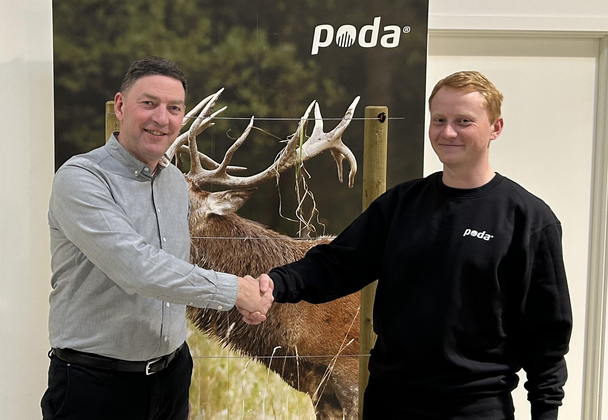 Poda-direktør Peter giver hånd til Sofus fra det nye Poda-center, Poda Hegn Ringe, foran et banner med kronhjort og elhegn.