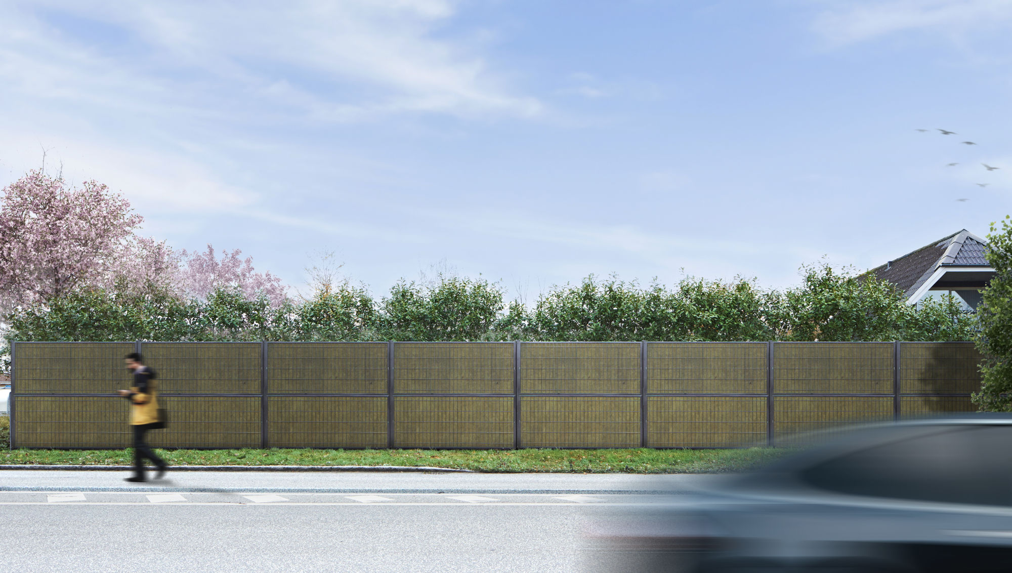 Noistop Essential støjhegn med antracitgrå ramme, omgivet af grøn beplantning, med en fodgænger og en forbipasserende bil i forgrunden.