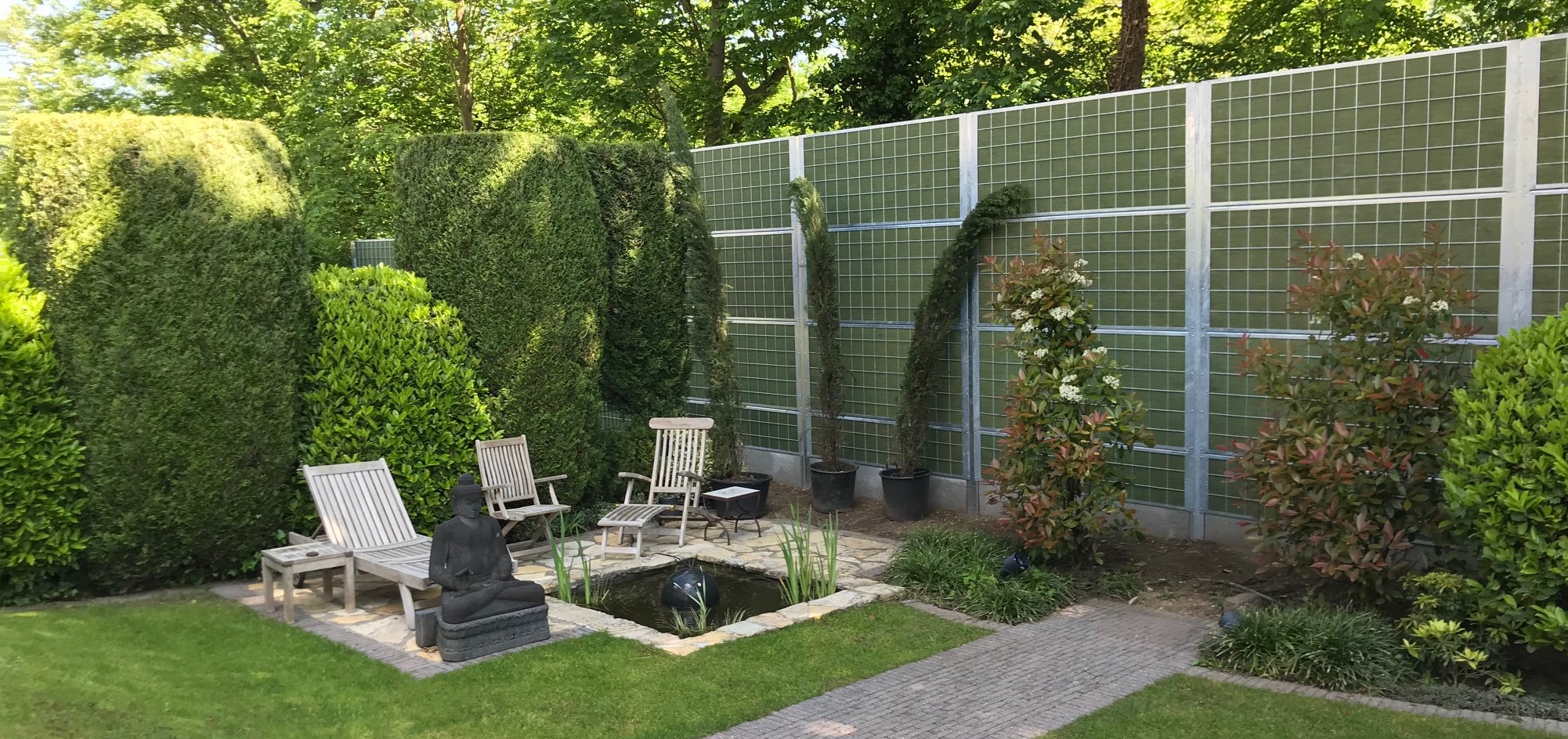 En hyggelig have med buske og en lille fiskedam afskærmet fra nabostøj med et Noistop® Steel støjhegn fra Poda Hegn