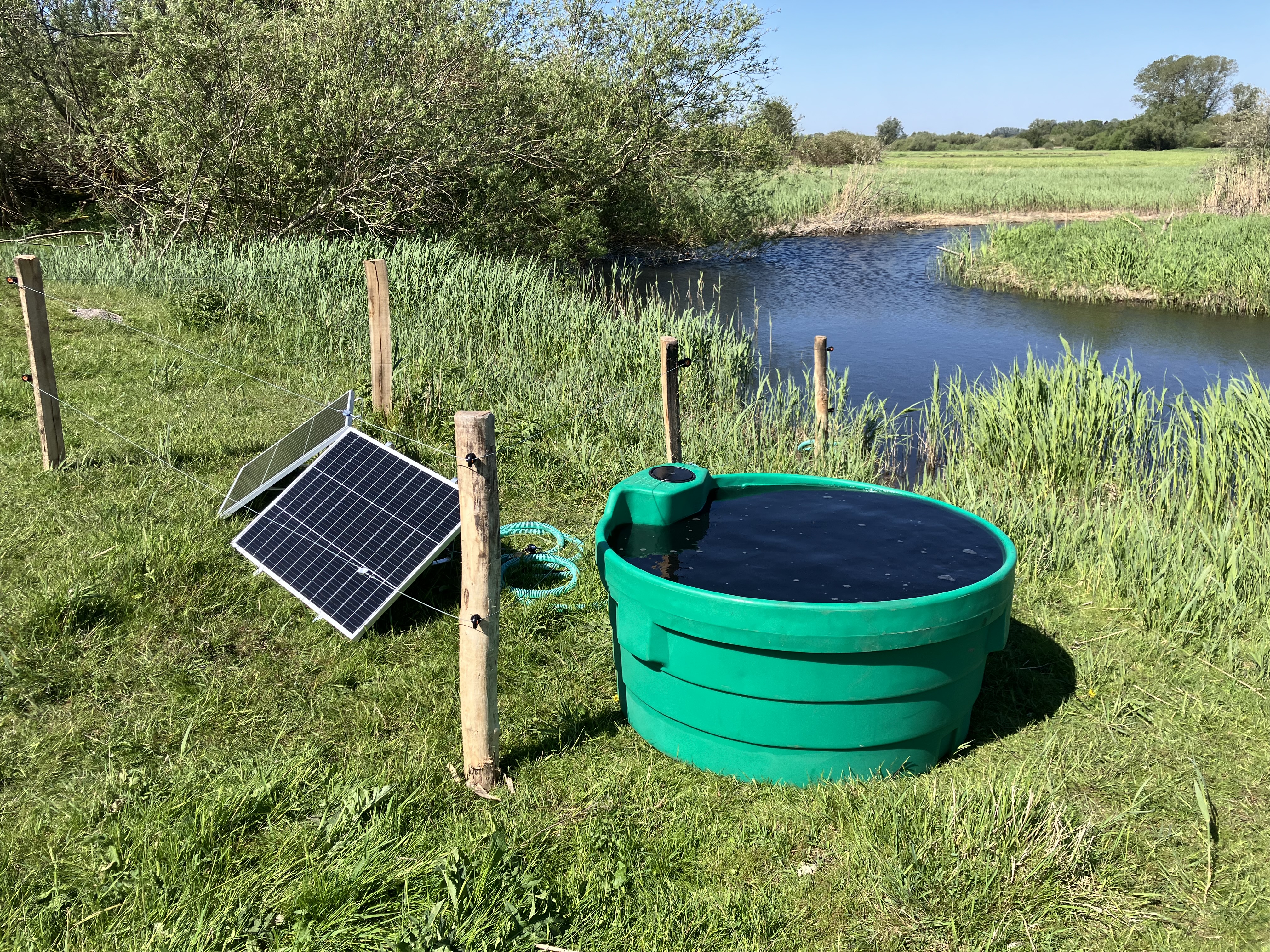 Soldrevet markpumpe med solpanel og vandkar ved en å på en græsmark