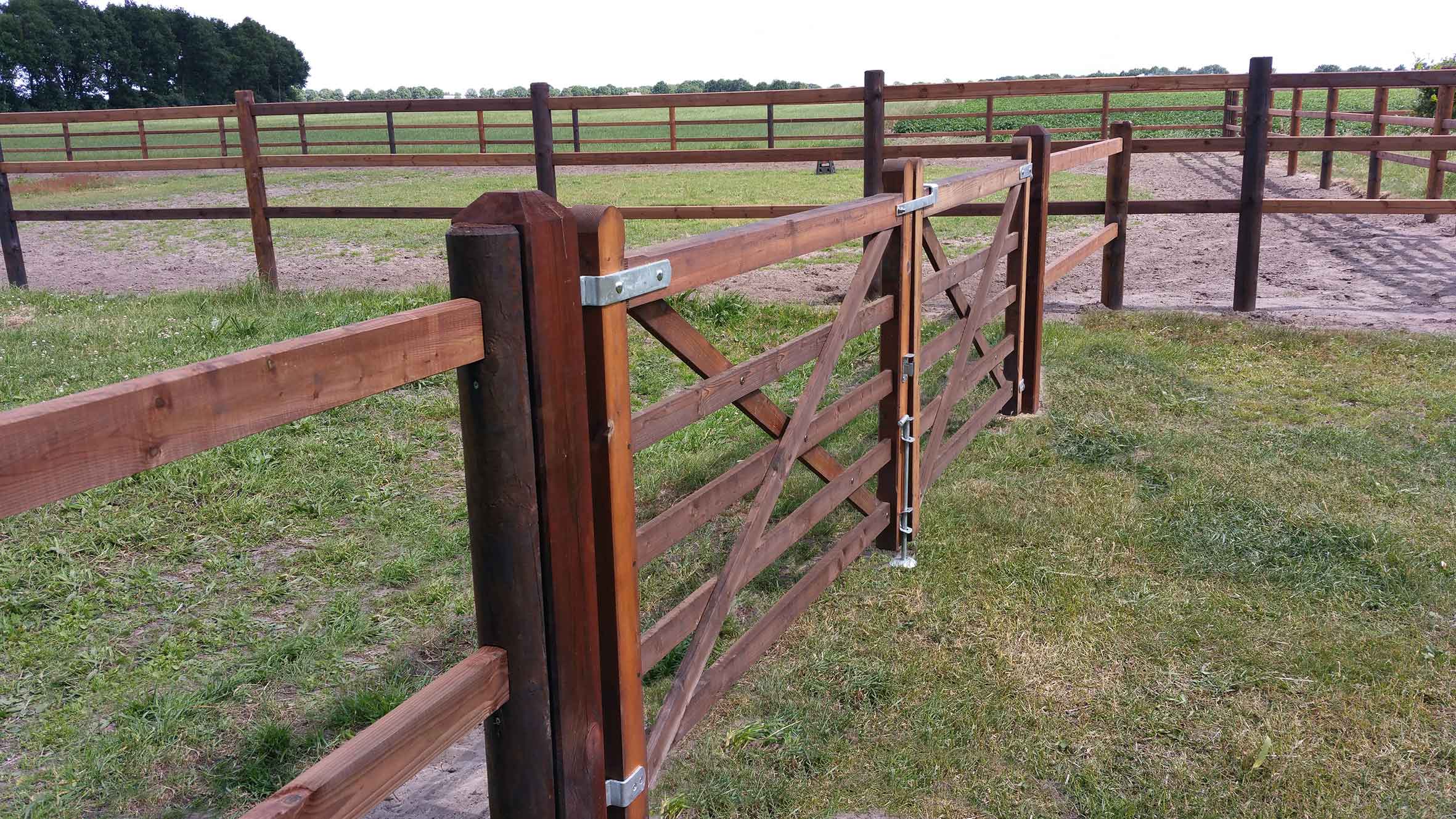 Et hestehegn afgrænser to hestefolde fra hinanden. En dobbelt trælåge giver adgang til den ene hestefold.