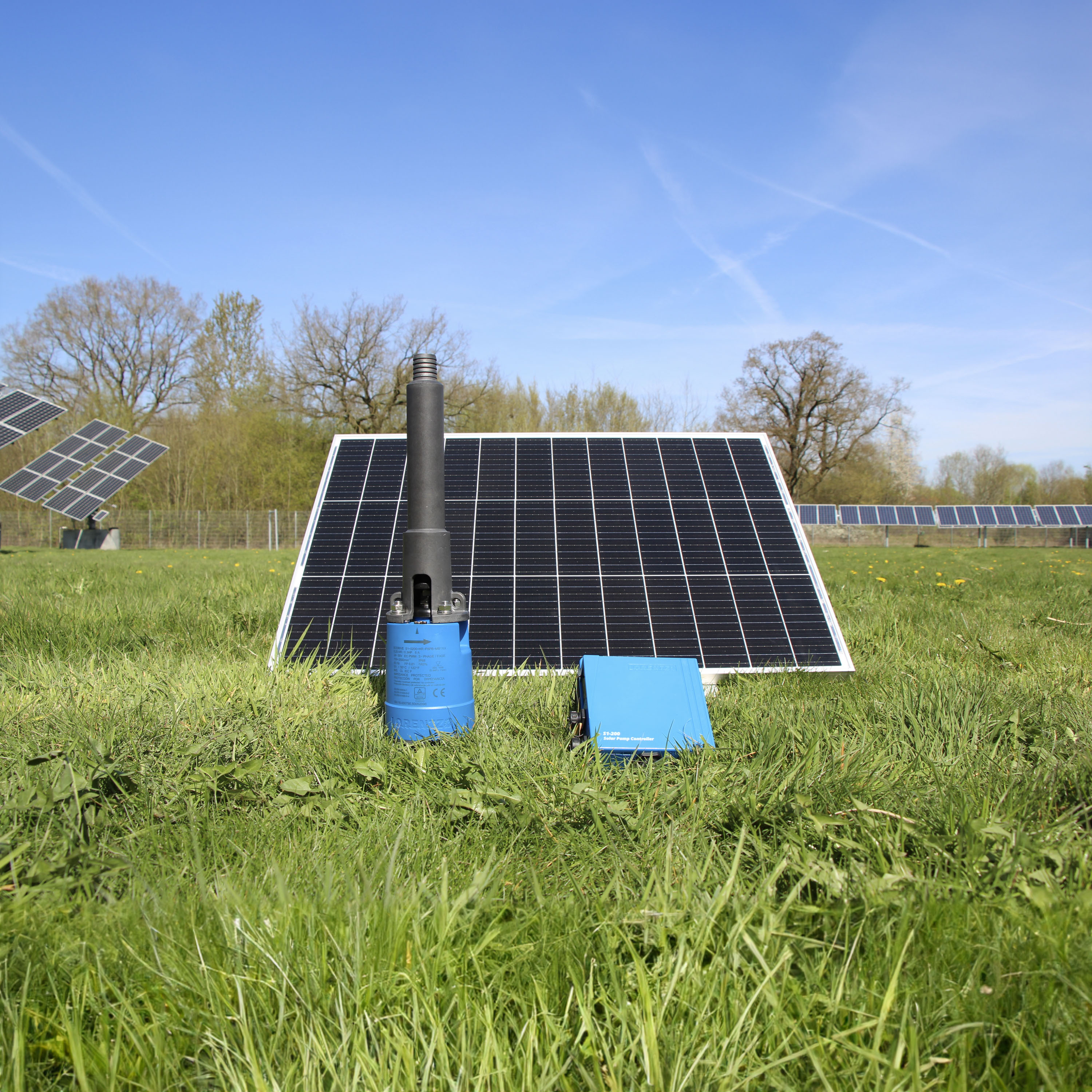 Solcelledrevet pumpe med solpanel og kontrolenhed på en grøn mark.
