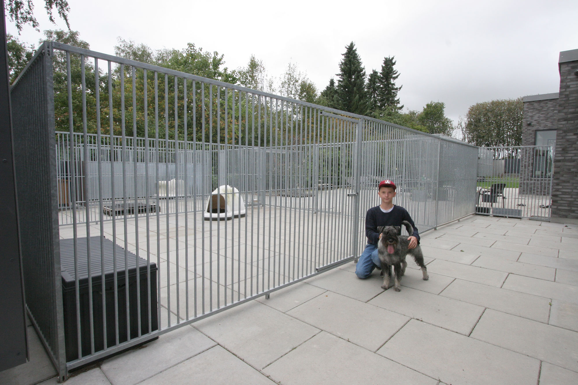 En dreng sidder på knæ foran en hundegård sammen med hans hund.