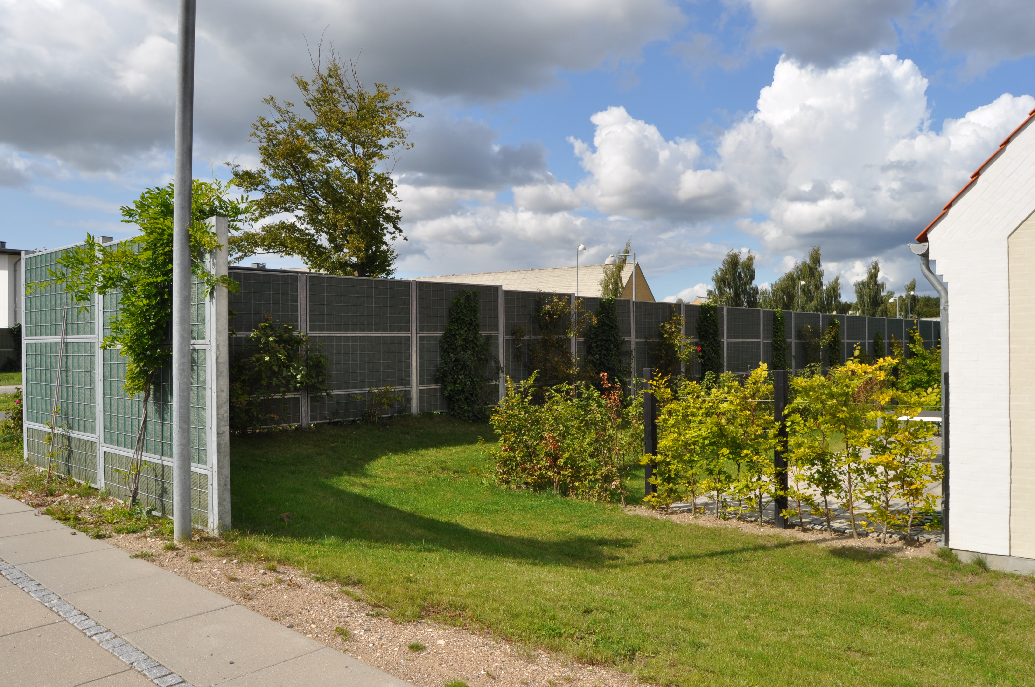 Noistop Steel støjhegn fra ROCKWOOL opsat i et grønt bymiljø med beplantning.
