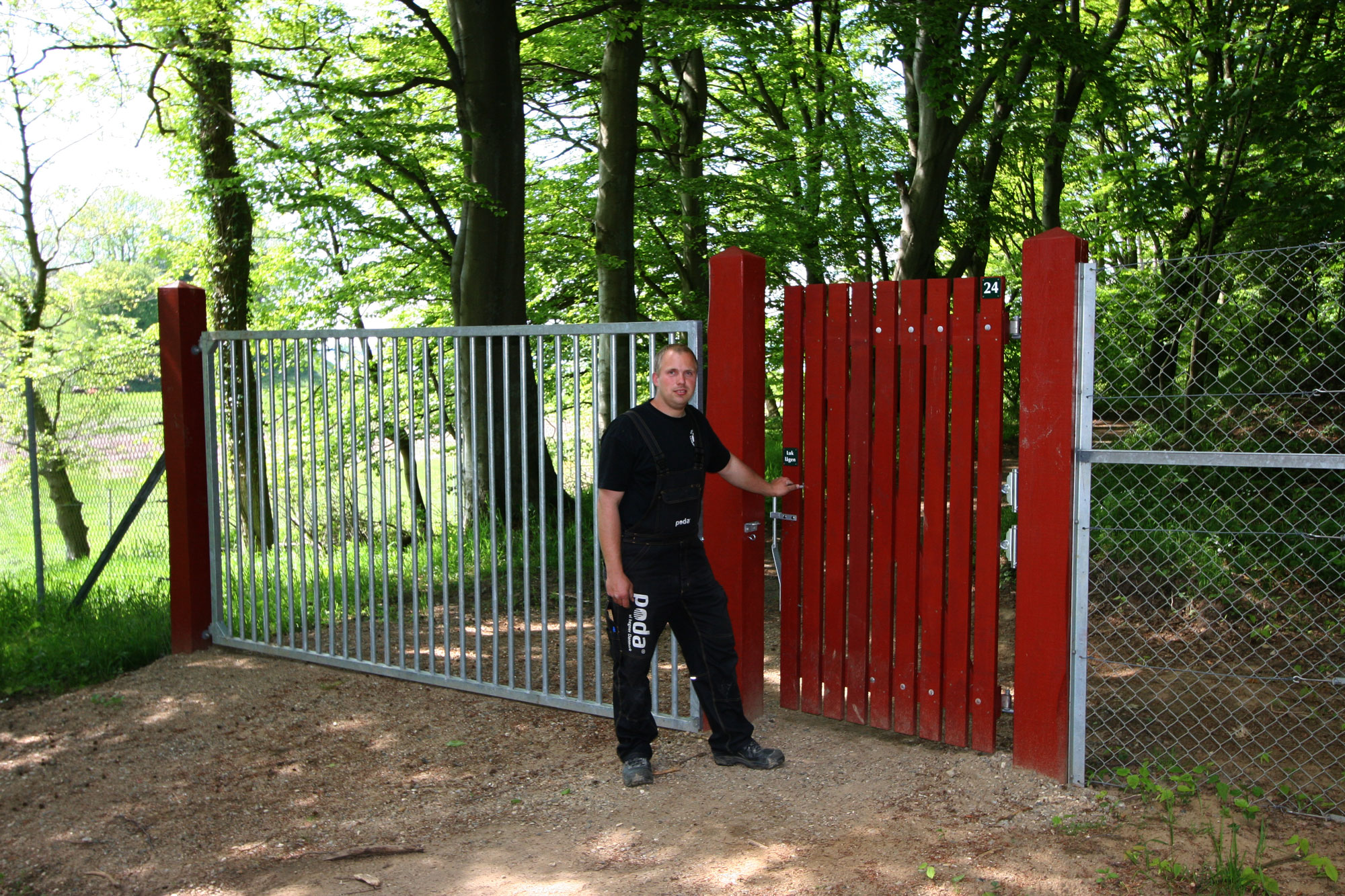 En mand står foran en rød trælåge, der fører ind til en dyrehave. Ved siden af lågen ses en port i stål.